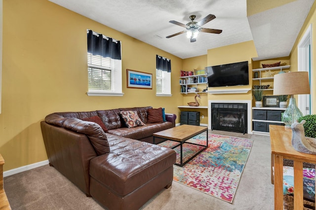 carpeted living area with a fireplace with flush hearth, a textured ceiling, baseboards, and a ceiling fan