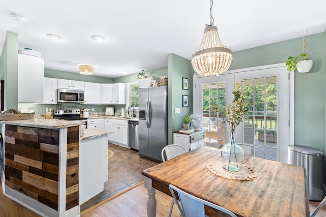 kitchen featuring appliances with stainless steel finishes, decorative light fixtures, a peninsula, white cabinetry, and a sink