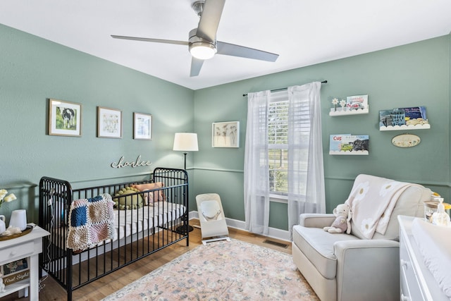 bedroom featuring wood finished floors, a ceiling fan, visible vents, baseboards, and a crib