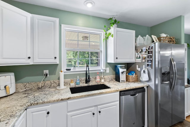 kitchen with light stone counters, white cabinetry, stainless steel appliances, and a sink