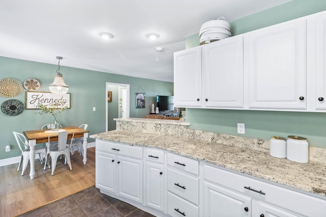 kitchen featuring a peninsula, white cabinetry, pendant lighting, and light stone counters