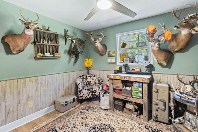 rec room with ceiling fan, a wainscoted wall, wood walls, and wood finished floors