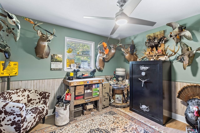 interior space with ceiling fan, a wainscoted wall, wood walls, and wood finished floors