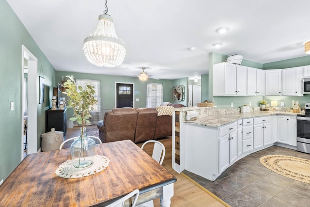 kitchen with appliances with stainless steel finishes, light stone countertops, white cabinetry, and ceiling fan with notable chandelier