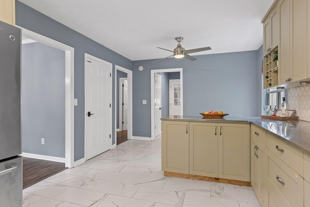 kitchen featuring kitchen peninsula, backsplash, ceiling fan, cream cabinets, and stainless steel refrigerator