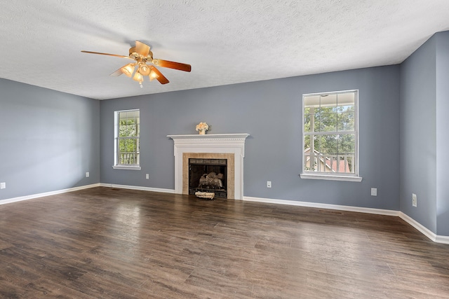 unfurnished living room featuring a tile fireplace, ceiling fan, dark wood-type flooring, and a textured ceiling