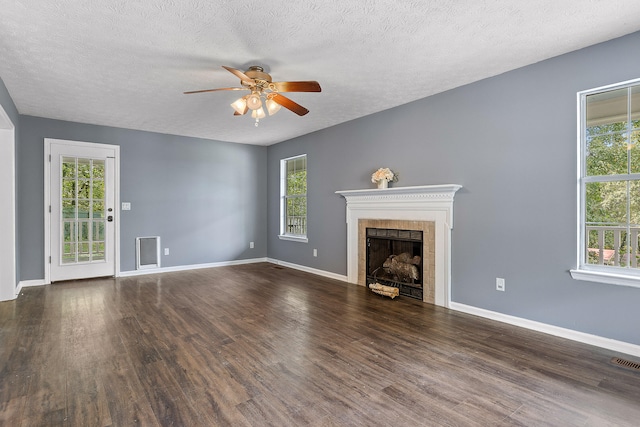 unfurnished living room featuring a tile fireplace, a textured ceiling, dark hardwood / wood-style flooring, and ceiling fan