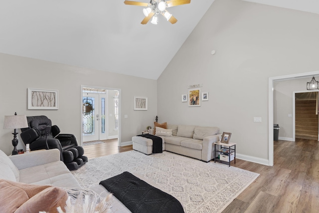 living area with a ceiling fan, wood finished floors, high vaulted ceiling, baseboards, and stairs