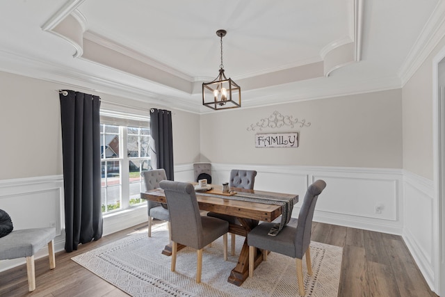 dining room featuring a wainscoted wall, a tray ceiling, wood finished floors, and ornamental molding