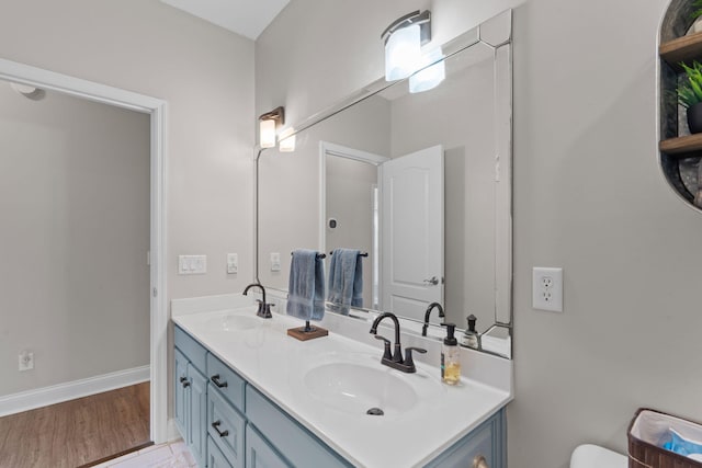 full bath featuring double vanity, wood finished floors, a sink, and baseboards