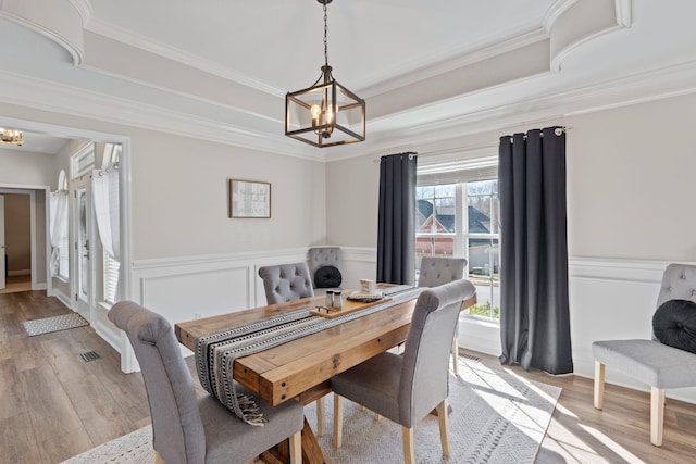 dining space with a wainscoted wall, light wood-style flooring, a chandelier, and ornamental molding