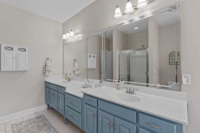 full bath with double vanity, a sink, a shower stall, baseboards, and tile patterned floors