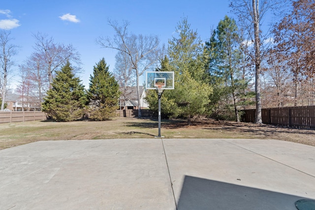view of basketball court featuring basketball hoop, a lawn, and fence