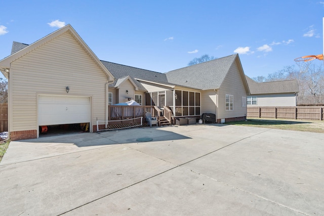 rear view of property featuring a garage, concrete driveway, fence, and a sunroom