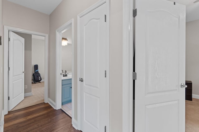 hallway with a sink, baseboards, and dark wood-type flooring