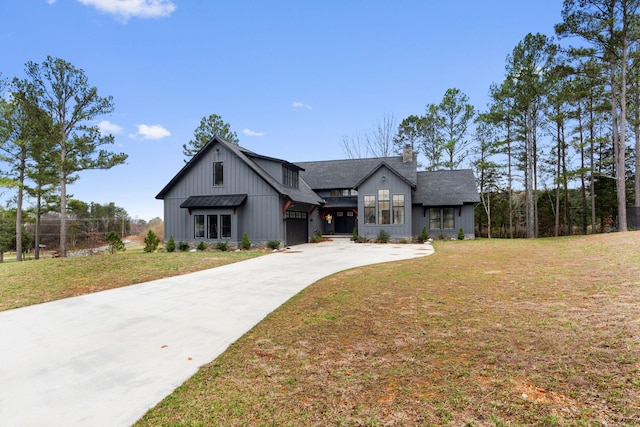 modern farmhouse with driveway, a front lawn, a chimney, and board and batten siding