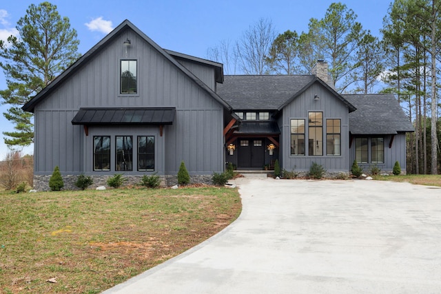 modern farmhouse style home featuring a shingled roof, a front yard, board and batten siding, a standing seam roof, and a chimney