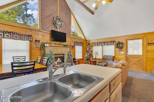 kitchen featuring high vaulted ceiling, dark colored carpet, sink, wooden walls, and a fireplace