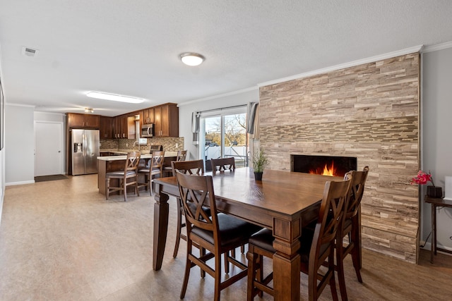 dining space with a large fireplace, ornamental molding, and a textured ceiling