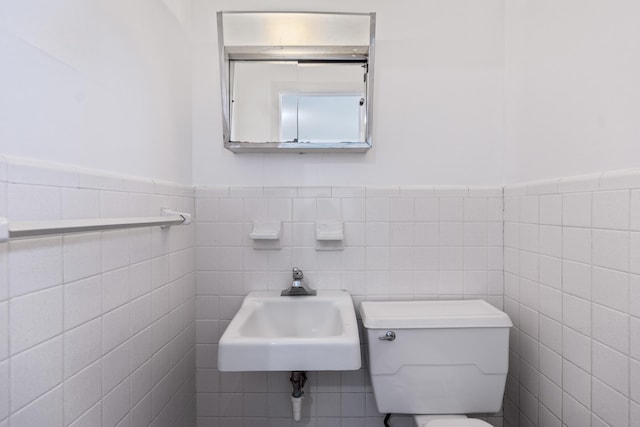 bathroom featuring toilet, tile walls, and sink