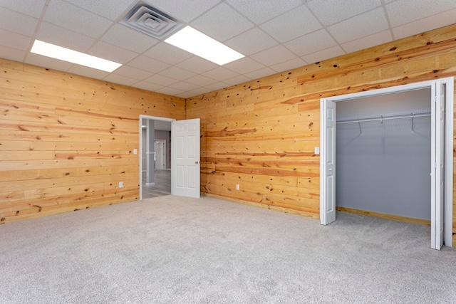 unfurnished bedroom featuring carpet, a paneled ceiling, wood walls, and a closet