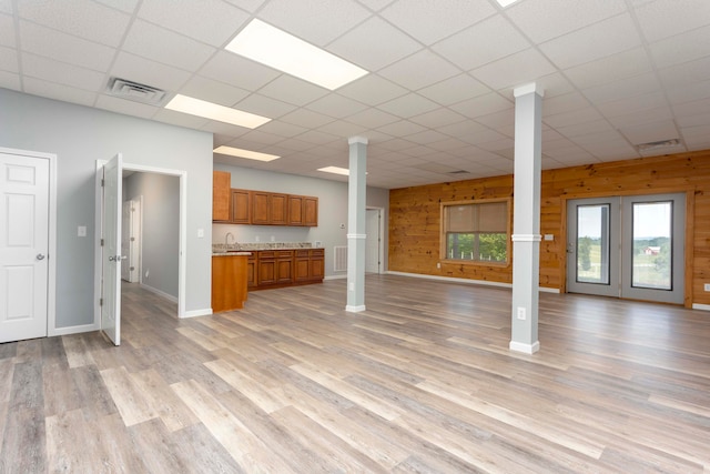 unfurnished living room featuring a paneled ceiling, light hardwood / wood-style floors, wooden walls, and sink