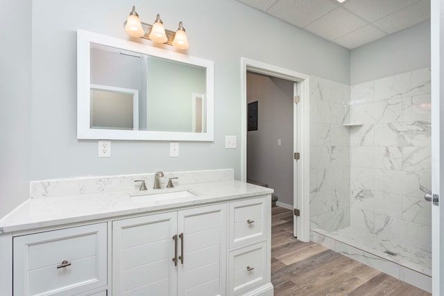 bathroom with vanity, a drop ceiling, wood-type flooring, and tiled shower