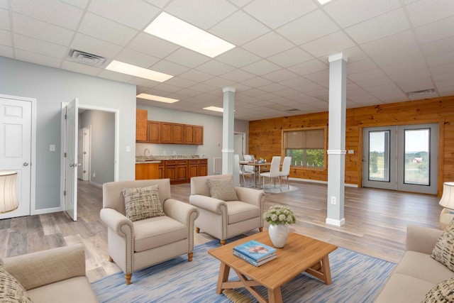 living room featuring a paneled ceiling, wood walls, light hardwood / wood-style flooring, and sink