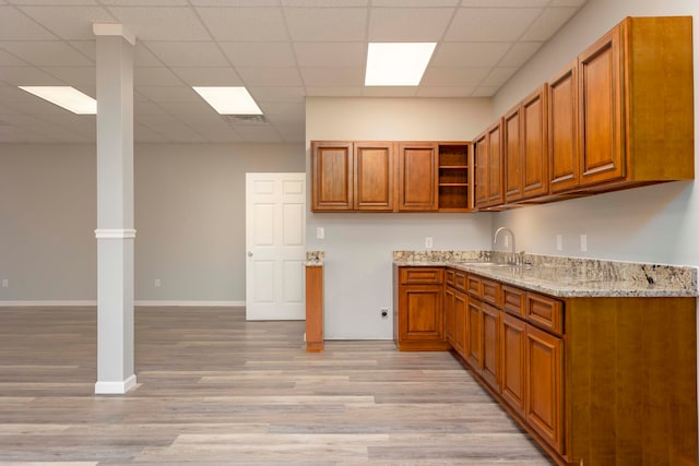 kitchen with a paneled ceiling, light stone counters, sink, and light wood-type flooring