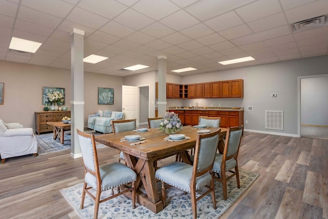 dining room featuring decorative columns, a paneled ceiling, sink, and light hardwood / wood-style floors