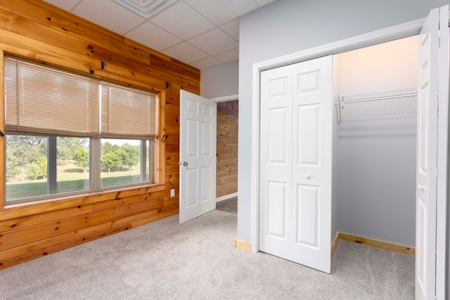 unfurnished bedroom featuring light carpet, a paneled ceiling, a closet, and wood walls