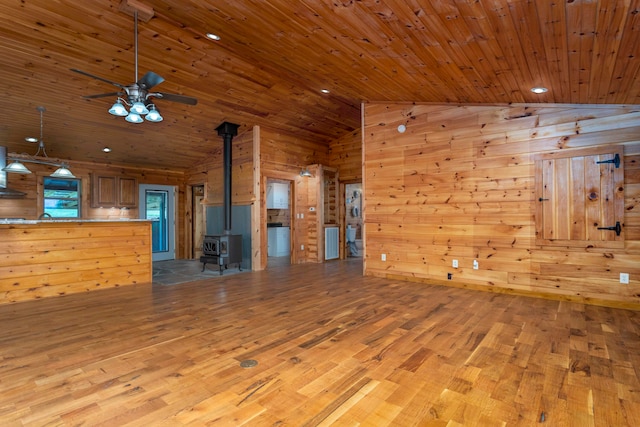 unfurnished living room with light hardwood / wood-style flooring, a wood stove, wooden ceiling, and wood walls