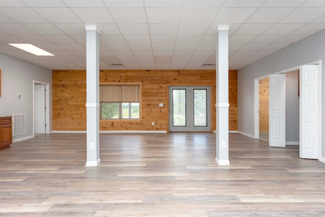 interior space featuring a paneled ceiling, wooden walls, and light hardwood / wood-style flooring