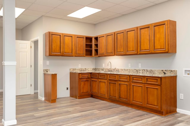 kitchen featuring a paneled ceiling, light stone countertops, sink, and light hardwood / wood-style floors