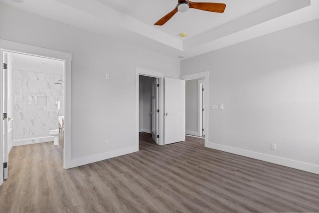 unfurnished bedroom with ceiling fan, dark hardwood / wood-style floors, a raised ceiling, and ensuite bath