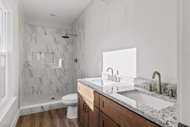 bathroom with hardwood / wood-style floors, vanity, toilet, and a tile shower