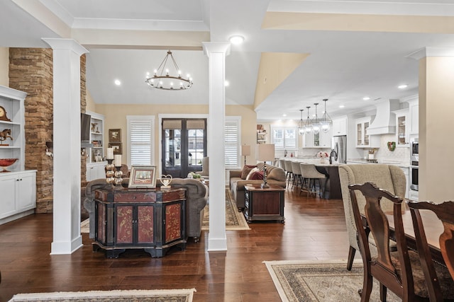 living room featuring dark wood-type flooring, a notable chandelier, ornamental molding, vaulted ceiling, and ornate columns