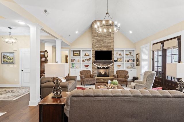 living room with an inviting chandelier, high vaulted ceiling, dark hardwood / wood-style floors, decorative columns, and a stone fireplace