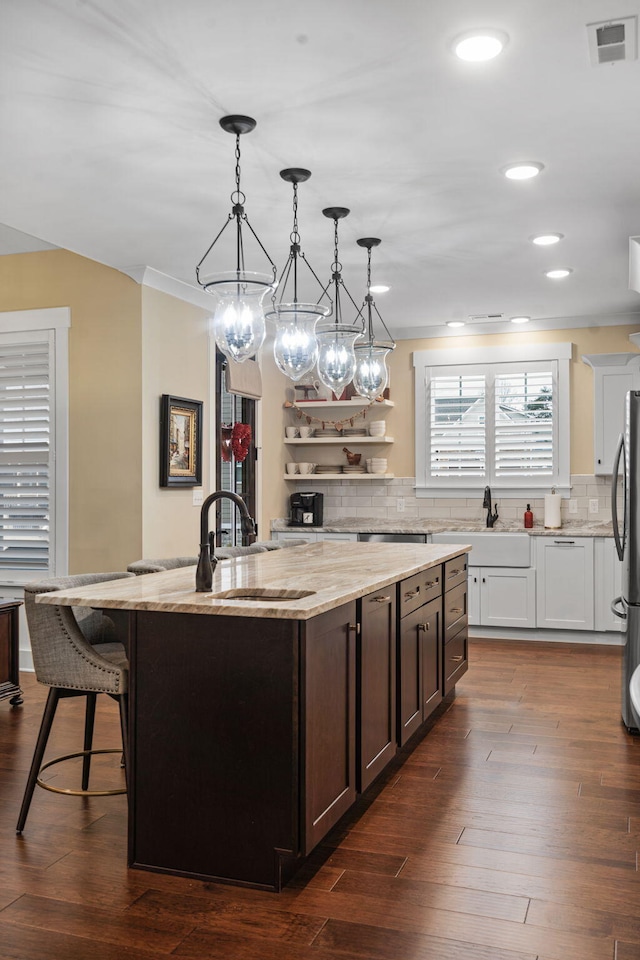 kitchen with hanging light fixtures, light stone countertops, a kitchen island with sink, and stainless steel refrigerator