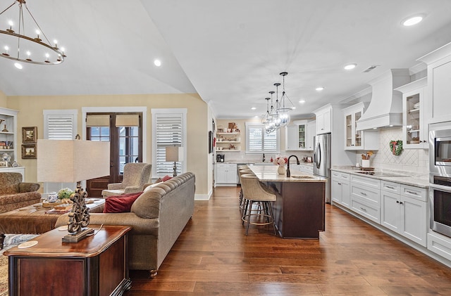 kitchen featuring light stone countertops, custom exhaust hood, hanging light fixtures, and a center island with sink