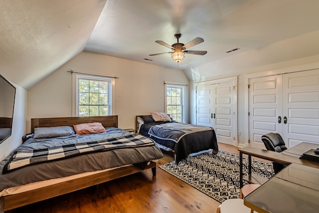 bedroom featuring lofted ceiling, hardwood / wood-style floors, ceiling fan, and two closets