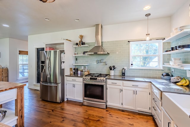 kitchen featuring white cabinetry, stainless steel appliances, decorative light fixtures, and wall chimney range hood