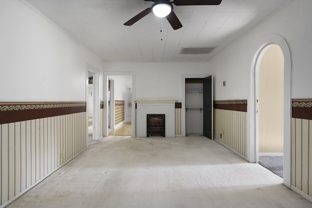 unfurnished living room featuring a fireplace, ceiling fan, ornamental molding, and light carpet