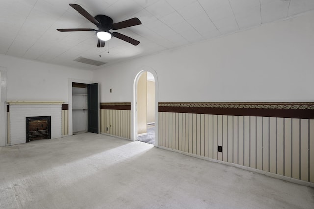 unfurnished living room with wood walls, ceiling fan, a fireplace, and light carpet