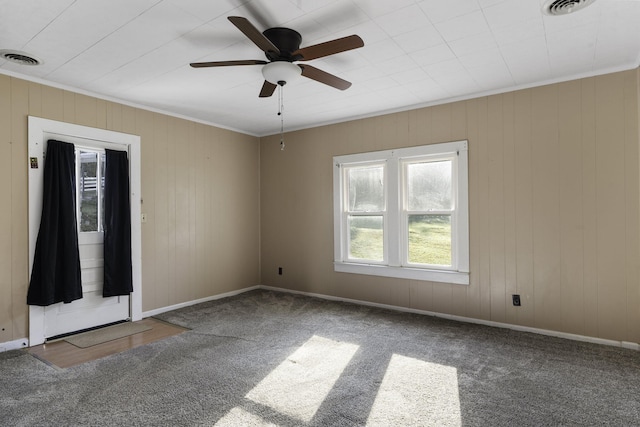 carpeted empty room featuring ceiling fan, crown molding, and wood walls