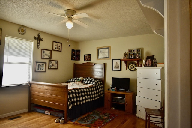 bedroom with ceiling fan, wood-type flooring, and a textured ceiling