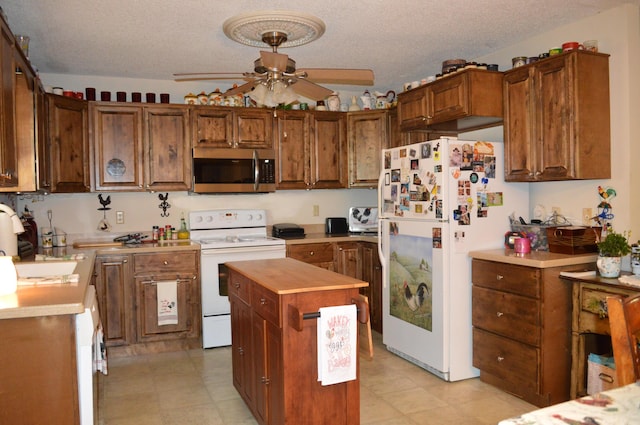 kitchen featuring white appliances, a textured ceiling, a center island, sink, and ceiling fan