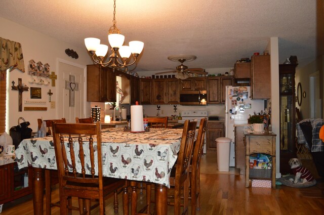 dining area with ceiling fan with notable chandelier, a textured ceiling, and wood-type flooring