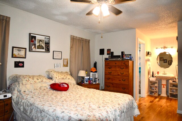 bedroom featuring ceiling fan, ensuite bath, a textured ceiling, and light hardwood / wood-style floors