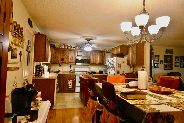 dining area with a textured ceiling, ceiling fan with notable chandelier, and light hardwood / wood-style flooring